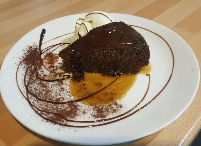 Sticky date pudding with butterscotch sauce and a scoop of ice cream on a white plate