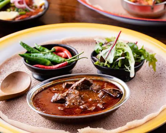 Zighini, lamb slow-cooked in berbere sauce, in a metal dish on injera with salad and green chillies