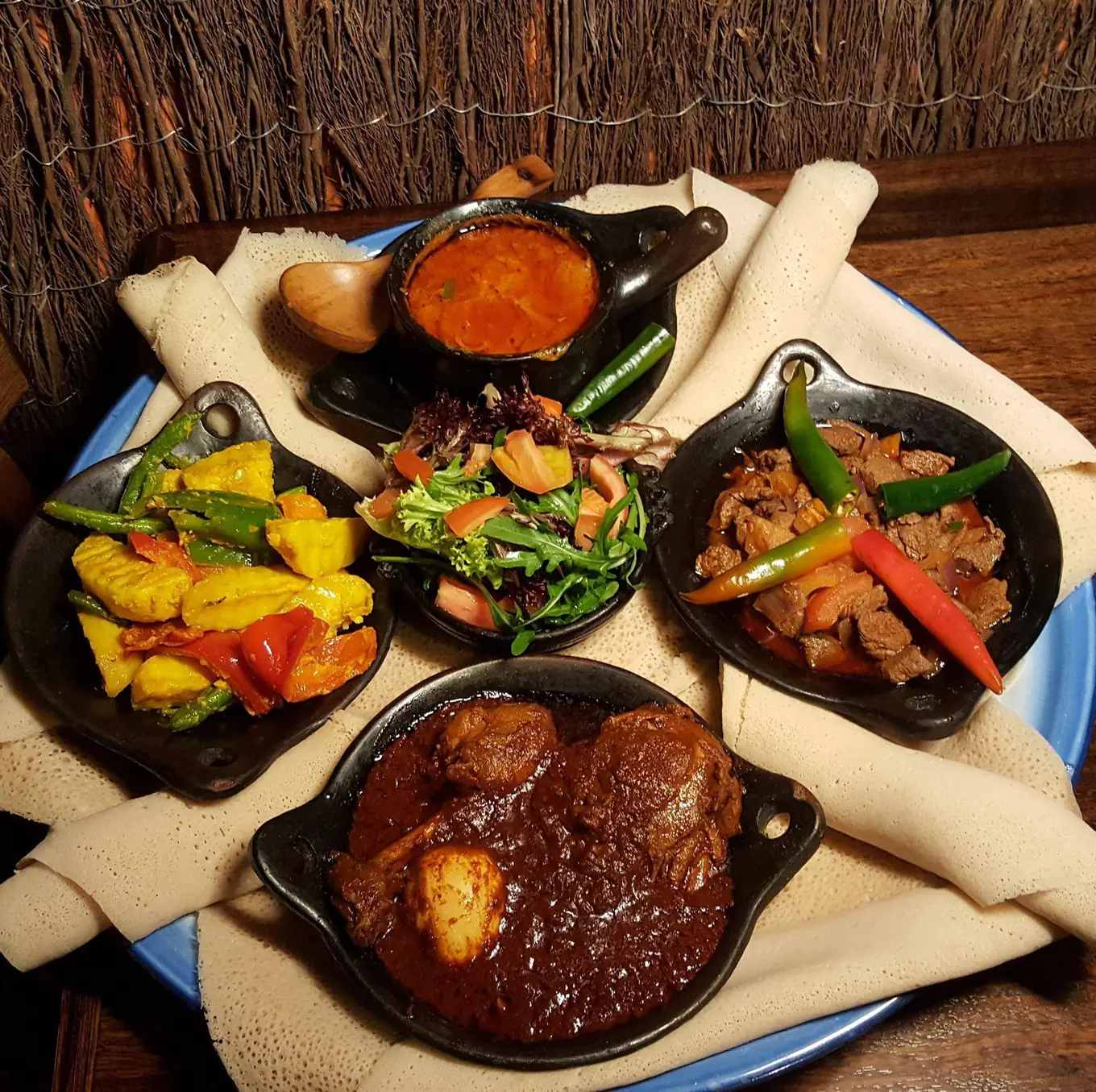 Dorho zighini with its egg, lamb with green chillies, yellow vegetables and salad in clay dishes on injera, from above