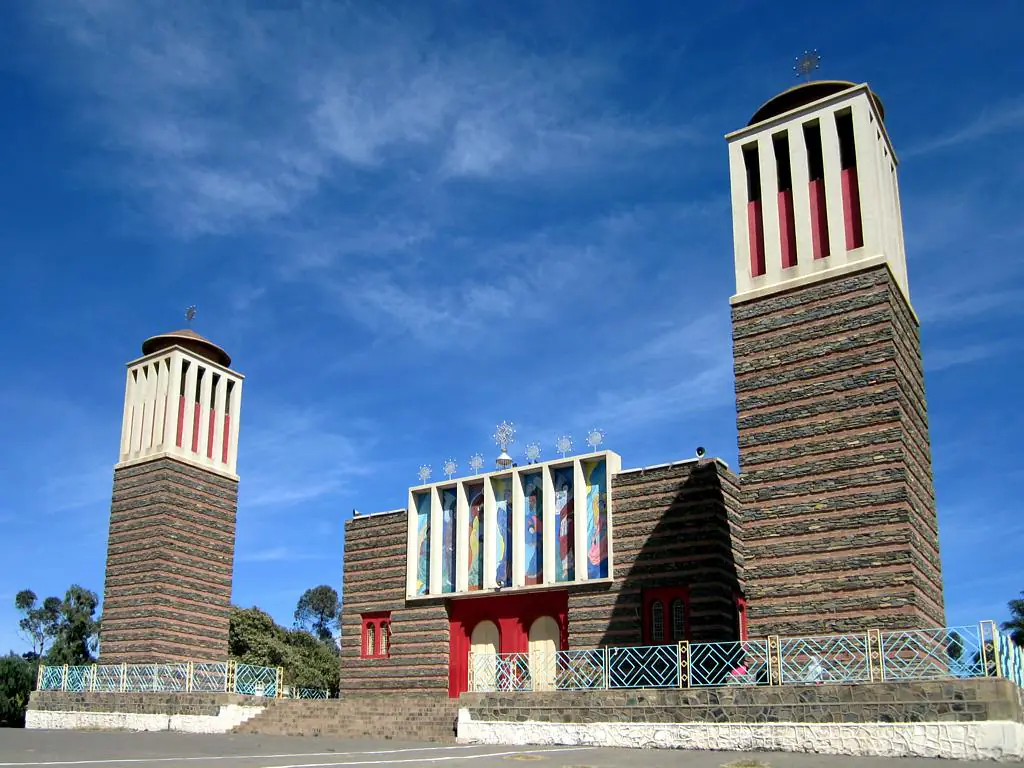 Enda Mariam Orthodox Cathedral in Asmara, a wide stone front with a tall bell tower and mosaic panels, under a blue sky