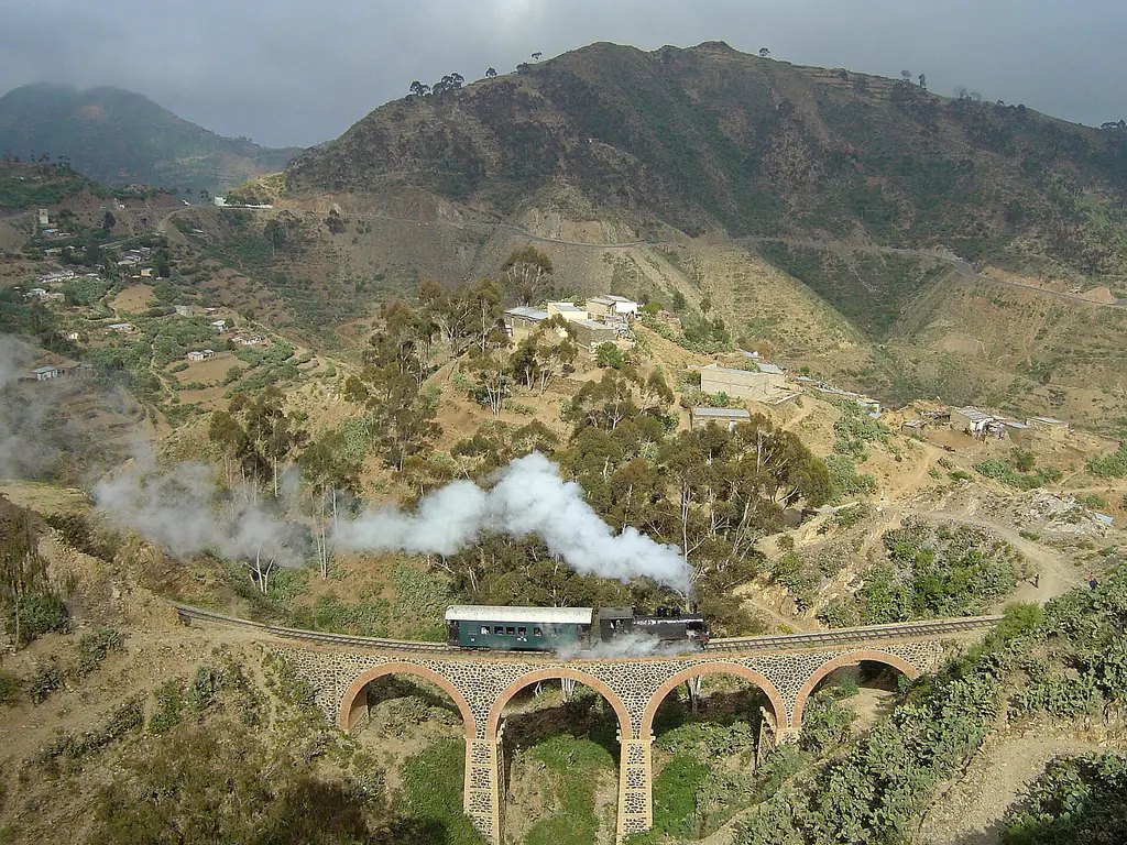 A small steam train crossing a stone viaduct on the mountain railway between Massawa and Asmara, with terraced hills behind