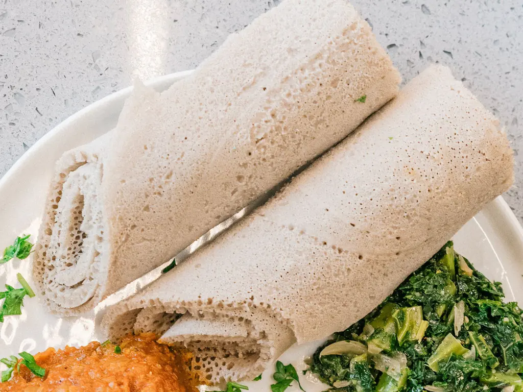 Three rolls of injera on a white plate, seen from above, showing the soft honeycomb surface