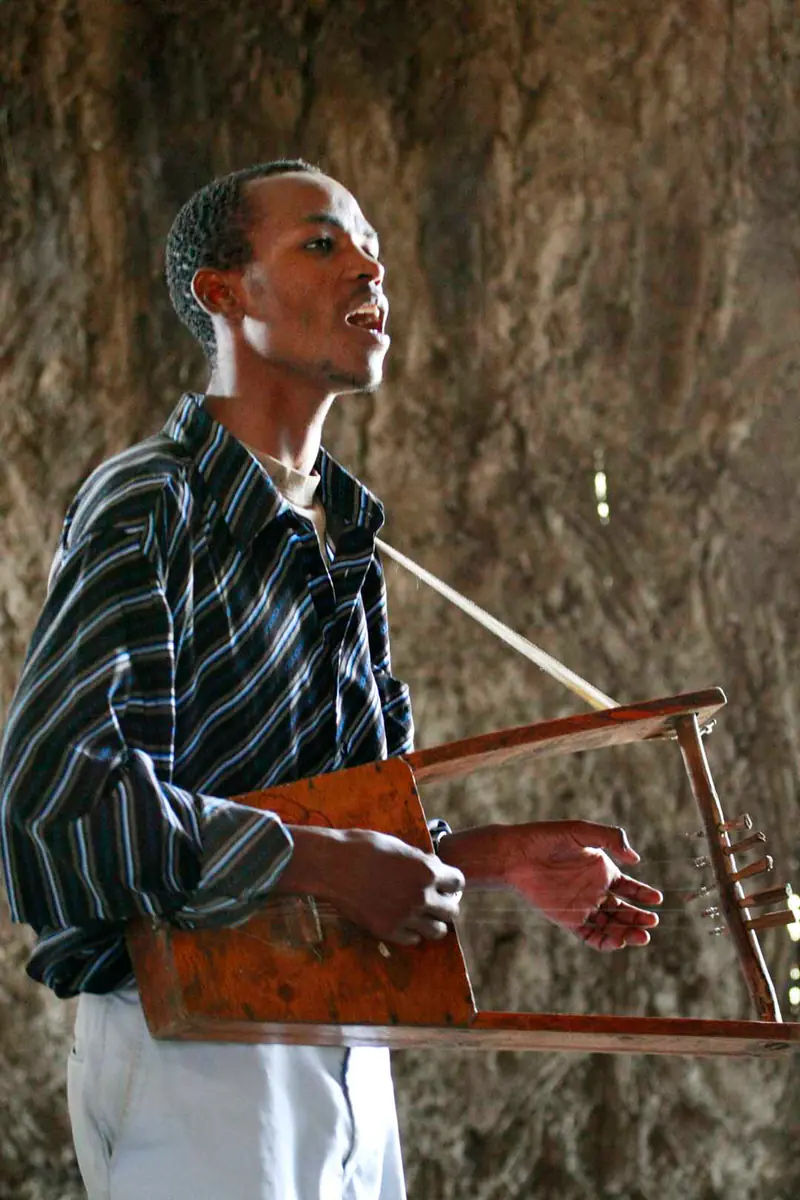 A young man singing as he plays a wooden six-string krar