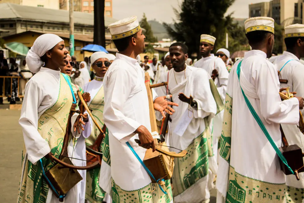 A line of musicians in white robes and embroidered sashes playing the one-string masenqo with bows at a Meskel procession