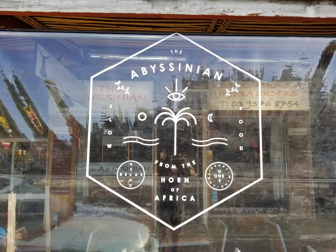 The new Abyssinian logo on the front window: a hexagon around a palm and the sea, with the words slow food from the Horn of Africa, relax, and one heart, one mind, one soul