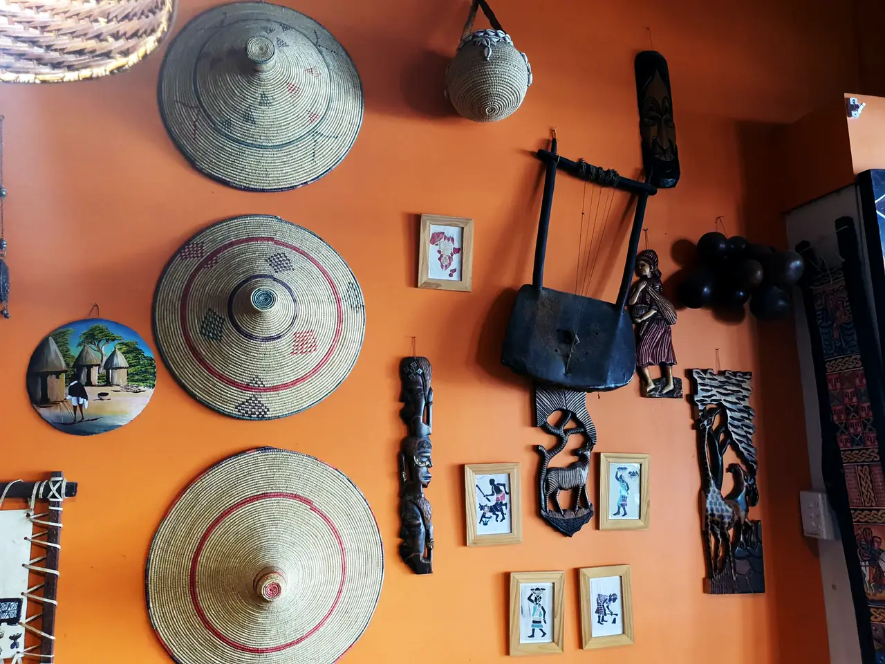 Woven baskets and lids, small paintings and carvings on the orange wall of the restaurant